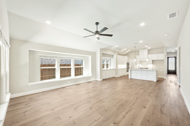 unfurnished living room with ceiling fan, a healthy amount of sunlight, sink, and light wood-type flooring