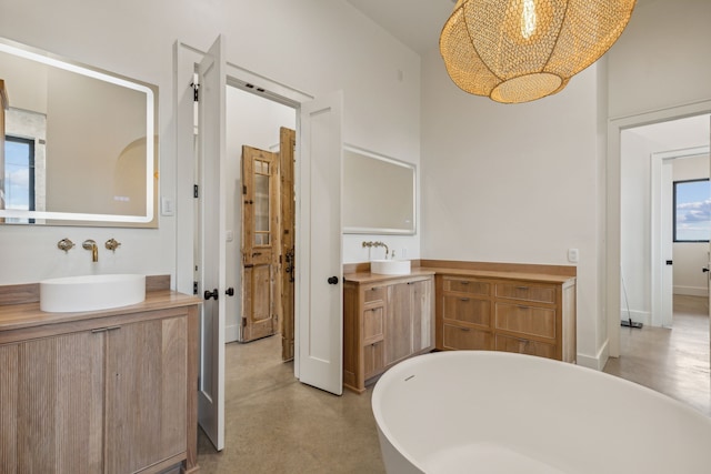 bathroom with a bath, concrete flooring, a wealth of natural light, and vanity