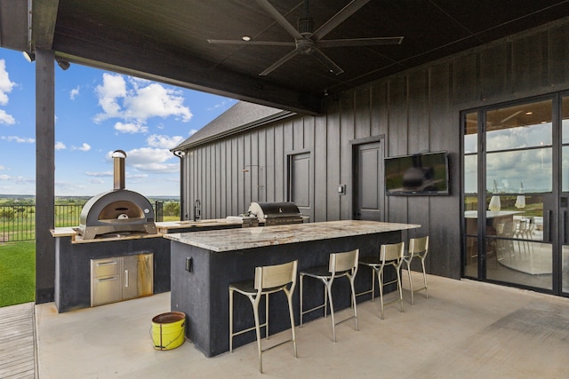 view of patio / terrace featuring exterior kitchen, grilling area, ceiling fan, and a wet bar