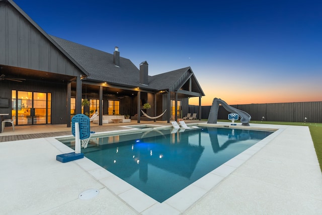 pool at dusk with a water slide, ceiling fan, and a patio