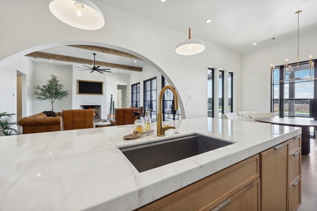 kitchen featuring hanging light fixtures, light brown cabinets, decorative backsplash, a kitchen island with sink, and sink