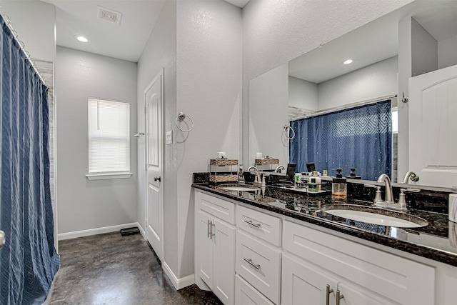 full bath with double vanity, concrete floors, baseboards, and a sink