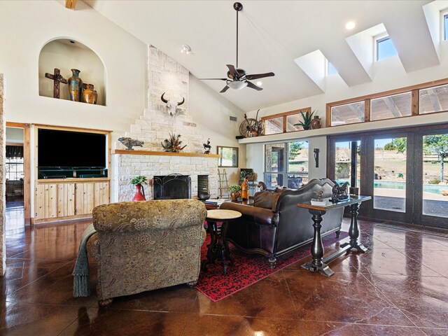 living room featuring a fireplace, ceiling fan, a skylight, and high vaulted ceiling