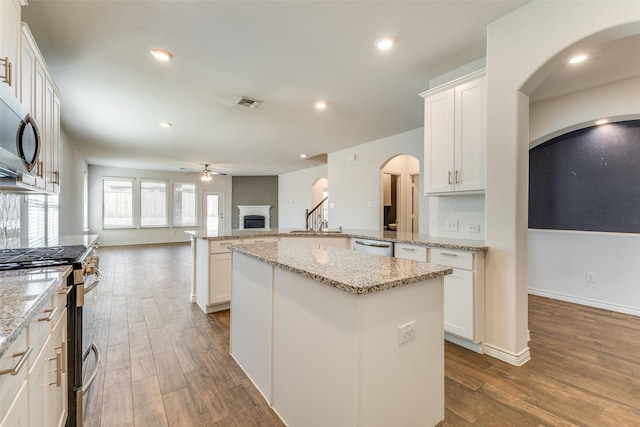 kitchen featuring ceiling fan, a center island, white cabinetry, appliances with stainless steel finishes, and light stone counters