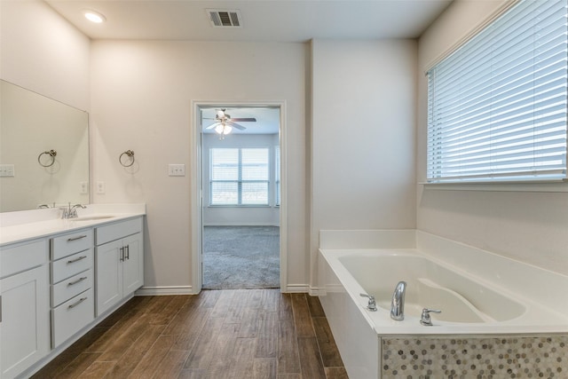 bathroom with ceiling fan, a relaxing tiled tub, and vanity