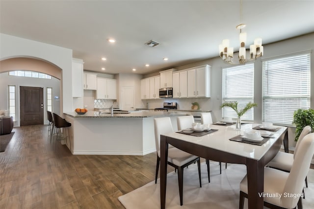 kitchen featuring appliances with stainless steel finishes, white cabinetry, dark hardwood / wood-style flooring, dark stone counters, and decorative backsplash