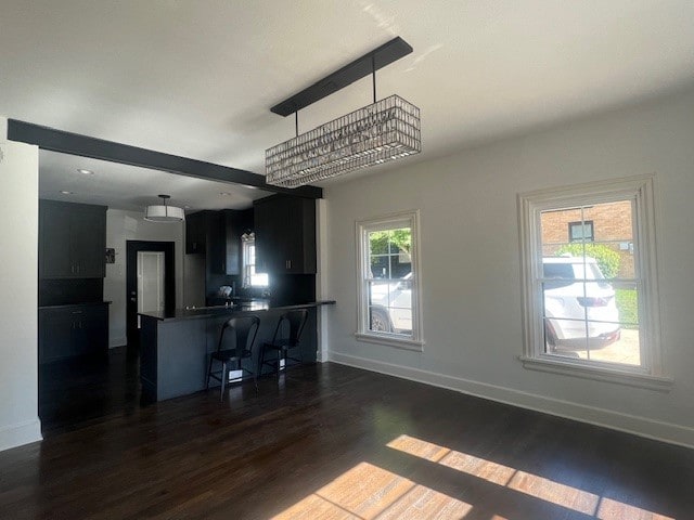 kitchen with dark wood-type flooring, a notable chandelier, kitchen peninsula, decorative light fixtures, and a breakfast bar area