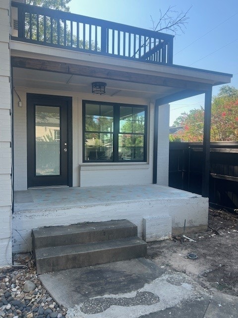 view of exterior entry featuring a balcony and covered porch