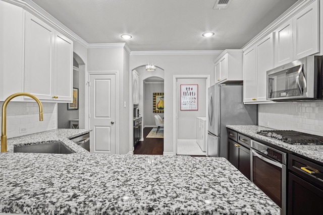 kitchen with sink, white cabinetry, ornamental molding, light stone countertops, and appliances with stainless steel finishes