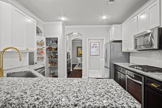 kitchen featuring light stone counters, stainless steel appliances, backsplash, ornamental molding, and sink