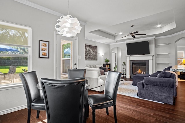 dining room featuring dark hardwood / wood-style flooring, a tile fireplace, a raised ceiling, and ceiling fan with notable chandelier