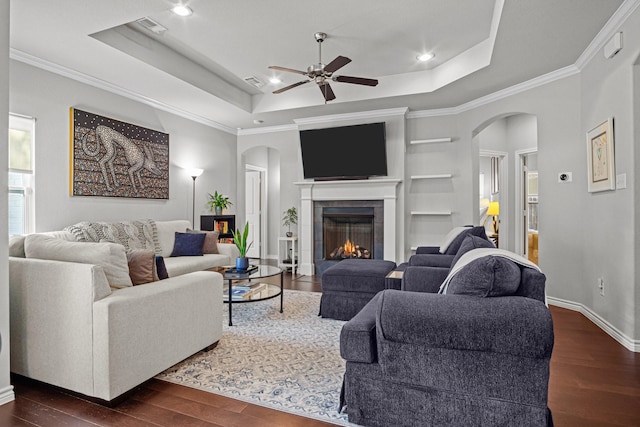 living room featuring ceiling fan, dark wood-type flooring, built in shelves, and a tray ceiling