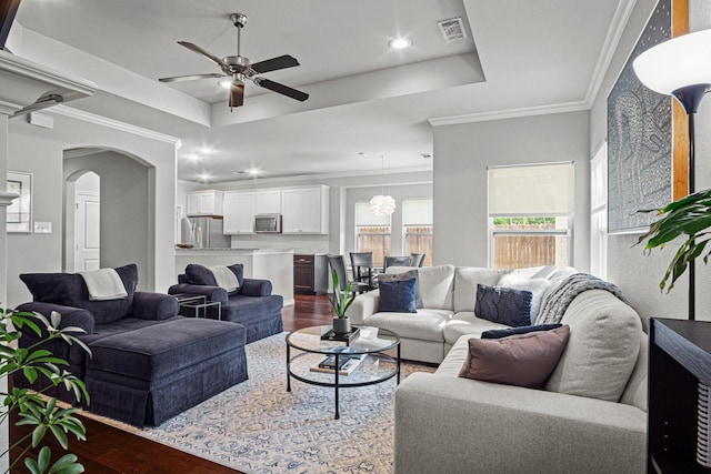 living room with a raised ceiling, ceiling fan, crown molding, and wood-type flooring