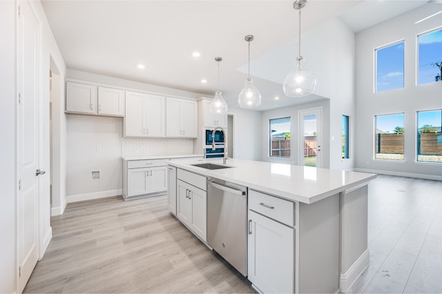 kitchen with a kitchen island with sink, hanging light fixtures, light hardwood / wood-style flooring, stainless steel dishwasher, and white cabinetry