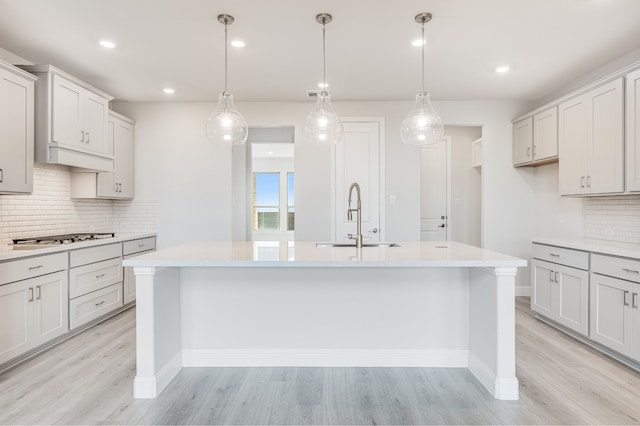 kitchen featuring sink, hanging light fixtures, a center island with sink, and light hardwood / wood-style flooring