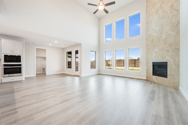 unfurnished living room featuring a fireplace, plenty of natural light, light hardwood / wood-style floors, and a high ceiling