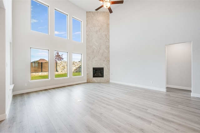 unfurnished living room featuring a high ceiling, light wood-type flooring, ceiling fan, and a premium fireplace