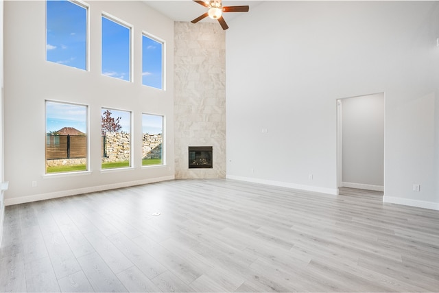 unfurnished living room featuring a fireplace, a high ceiling, light wood-type flooring, and ceiling fan