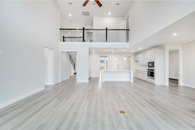 unfurnished living room with ceiling fan, sink, light hardwood / wood-style floors, and a high ceiling