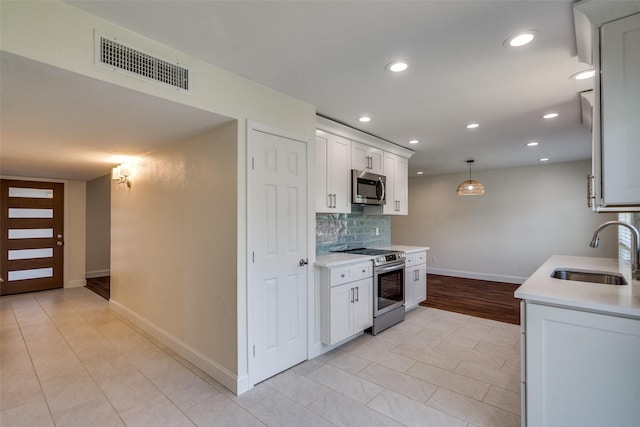 kitchen featuring appliances with stainless steel finishes, hanging light fixtures, decorative backsplash, white cabinets, and sink