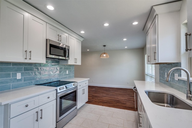 kitchen with stainless steel appliances, sink, white cabinets, light stone counters, and hanging light fixtures