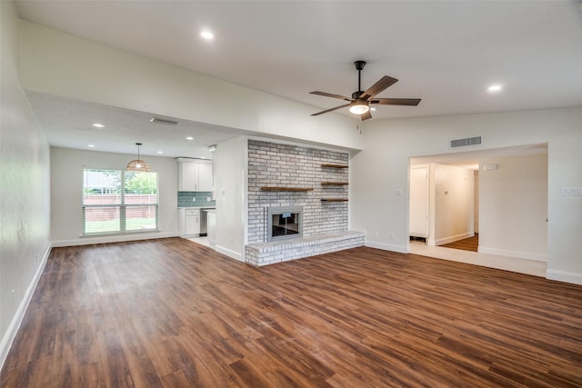 unfurnished living room with a brick fireplace, ceiling fan, vaulted ceiling, and dark hardwood / wood-style floors