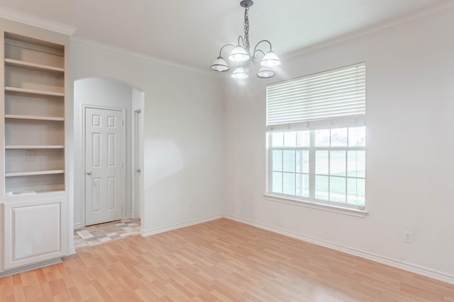 unfurnished room with arched walkways, light wood-style floors, ornamental molding, a chandelier, and baseboards