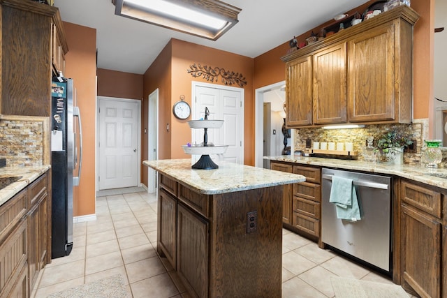 kitchen featuring a center island, stainless steel appliances, light stone counters, backsplash, and light tile patterned floors