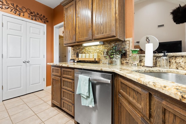 kitchen with dishwasher, sink, light stone counters, backsplash, and light tile patterned floors