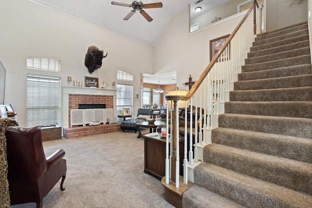 living room with carpet, a brick fireplace, ornamental molding, ceiling fan, and high vaulted ceiling