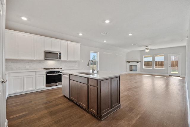 kitchen with appliances with stainless steel finishes, backsplash, a kitchen island with sink, white cabinets, and sink