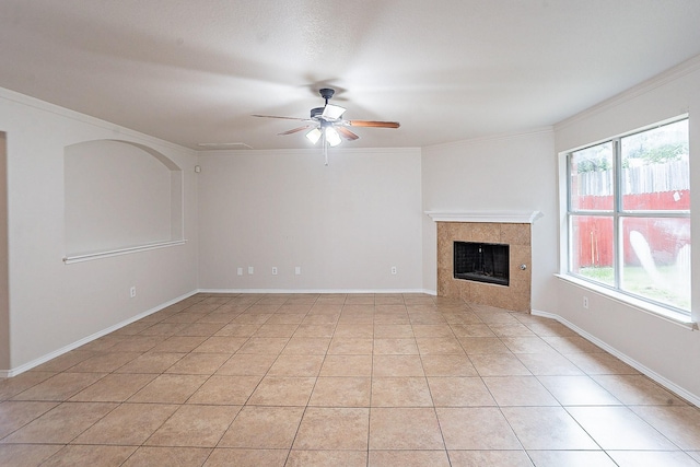 unfurnished living room with a tile fireplace, ceiling fan, plenty of natural light, light tile patterned flooring, and ornamental molding