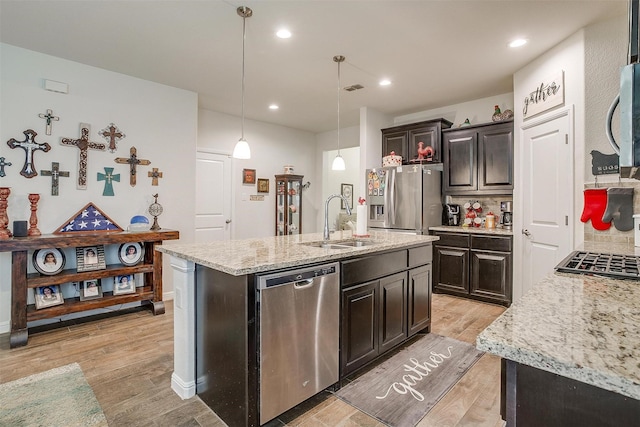 kitchen with a kitchen island with sink, sink, light wood-type flooring, decorative light fixtures, and stainless steel appliances