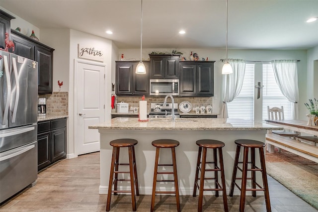 kitchen featuring backsplash, a kitchen island with sink, decorative light fixtures, and appliances with stainless steel finishes