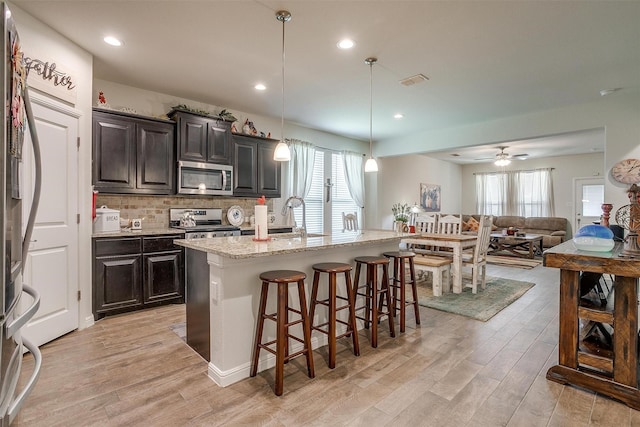 kitchen featuring sink, stainless steel appliances, decorative light fixtures, a kitchen bar, and a kitchen island with sink