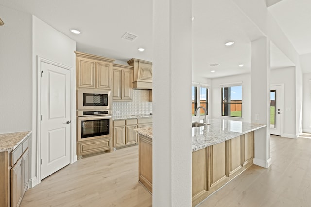 kitchen featuring light brown cabinetry, oven, light hardwood / wood-style flooring, and black microwave