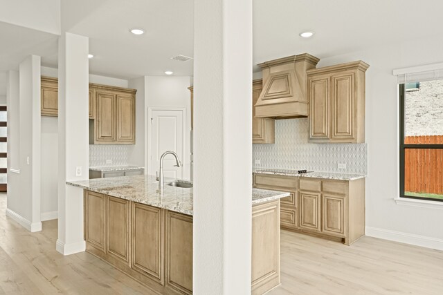 kitchen with light stone countertops, sink, backsplash, light hardwood / wood-style floors, and custom range hood