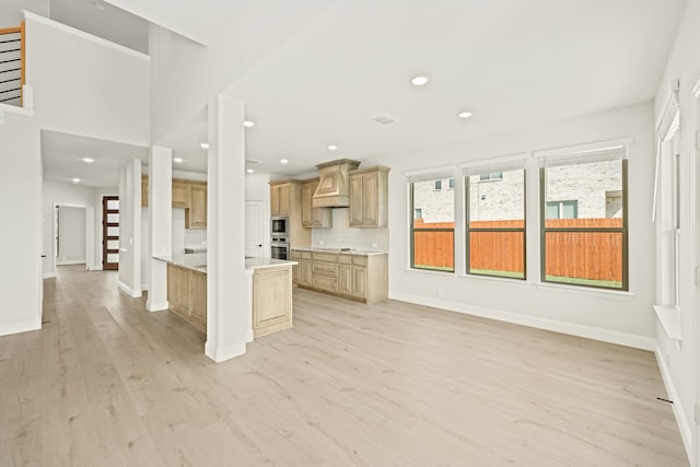 kitchen with kitchen peninsula, tasteful backsplash, appliances with stainless steel finishes, light brown cabinetry, and light hardwood / wood-style floors