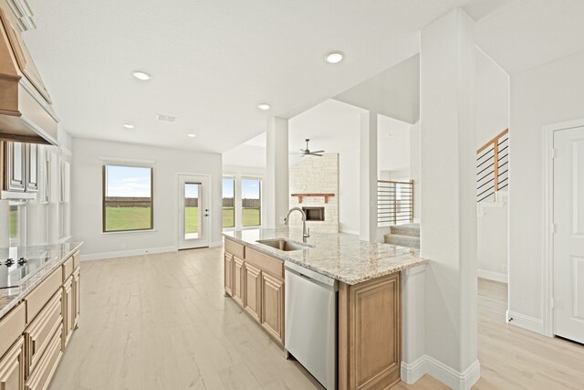 kitchen with dishwasher, a stone fireplace, light hardwood / wood-style flooring, sink, and light stone countertops