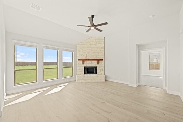 unfurnished living room with ceiling fan, a stone fireplace, lofted ceiling, and light wood-type flooring