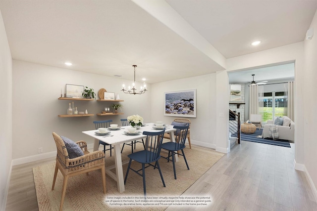 dining space featuring ceiling fan with notable chandelier, light hardwood / wood-style floors, and a brick fireplace