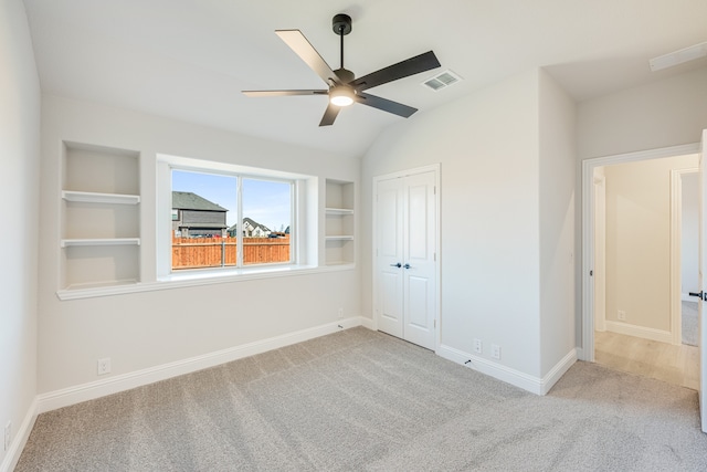 carpeted empty room featuring built in shelves, ceiling fan, and vaulted ceiling