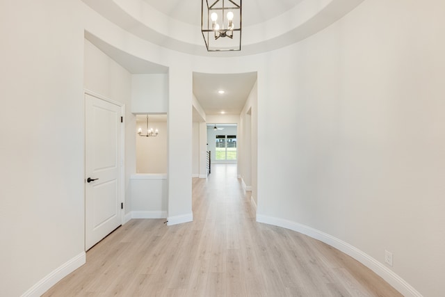 hall with light hardwood / wood-style floors, a raised ceiling, and a notable chandelier