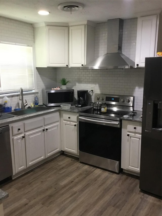 kitchen featuring decorative backsplash, white cabinetry, wall chimney range hood, and appliances with stainless steel finishes