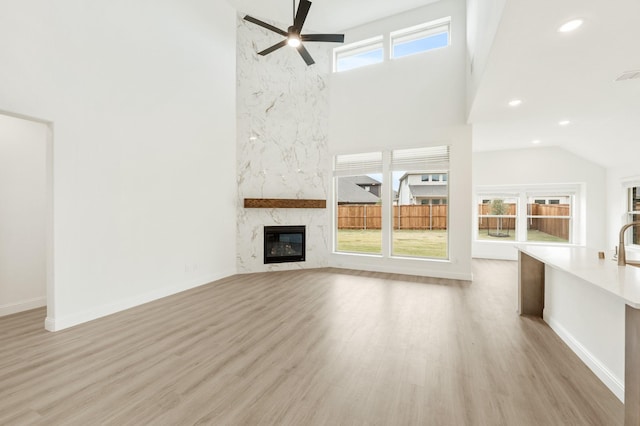 unfurnished living room featuring ceiling fan, a high end fireplace, a healthy amount of sunlight, and light wood-type flooring