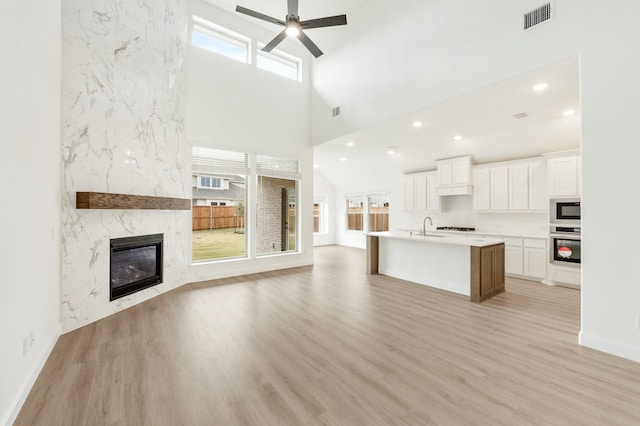 unfurnished living room featuring a high end fireplace, a high ceiling, sink, ceiling fan, and light wood-type flooring