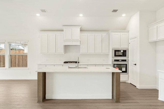 kitchen featuring a kitchen island with sink, oven, light wood-type flooring, white cabinetry, and black microwave