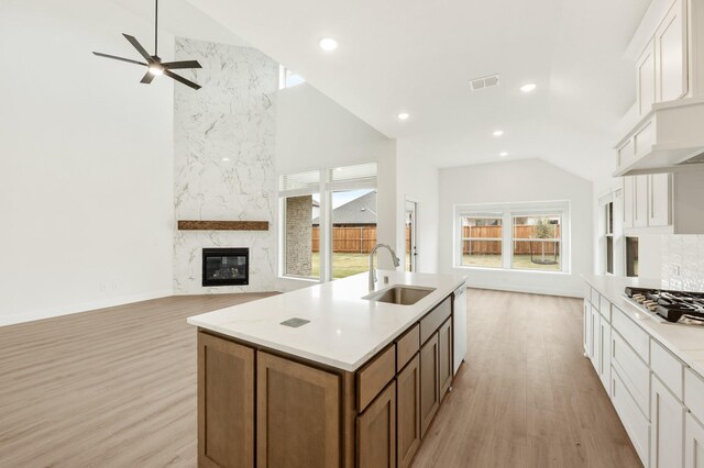 kitchen with white cabinetry, sink, stainless steel gas stovetop, a kitchen island with sink, and a fireplace