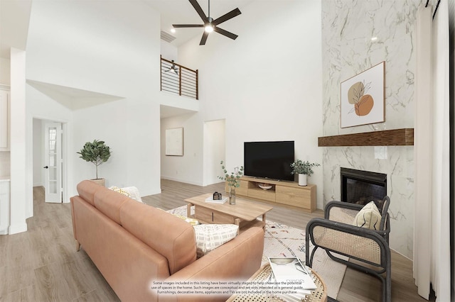 living room with ceiling fan, light wood-type flooring, a fireplace, and a high ceiling