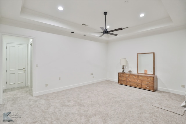 unfurnished bedroom with ceiling fan, a tray ceiling, and carpet